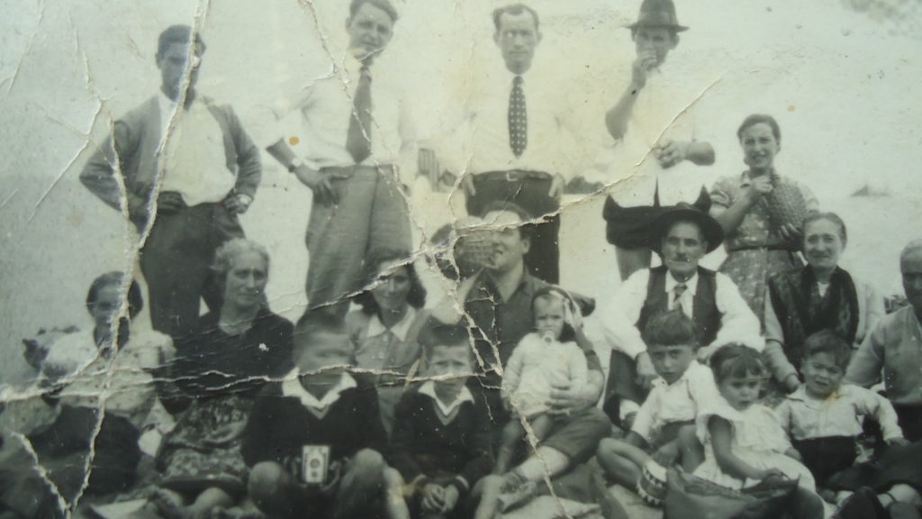 Fotografia antiga e gasta de um piquenique de família e amigos na praia nos anos 50.