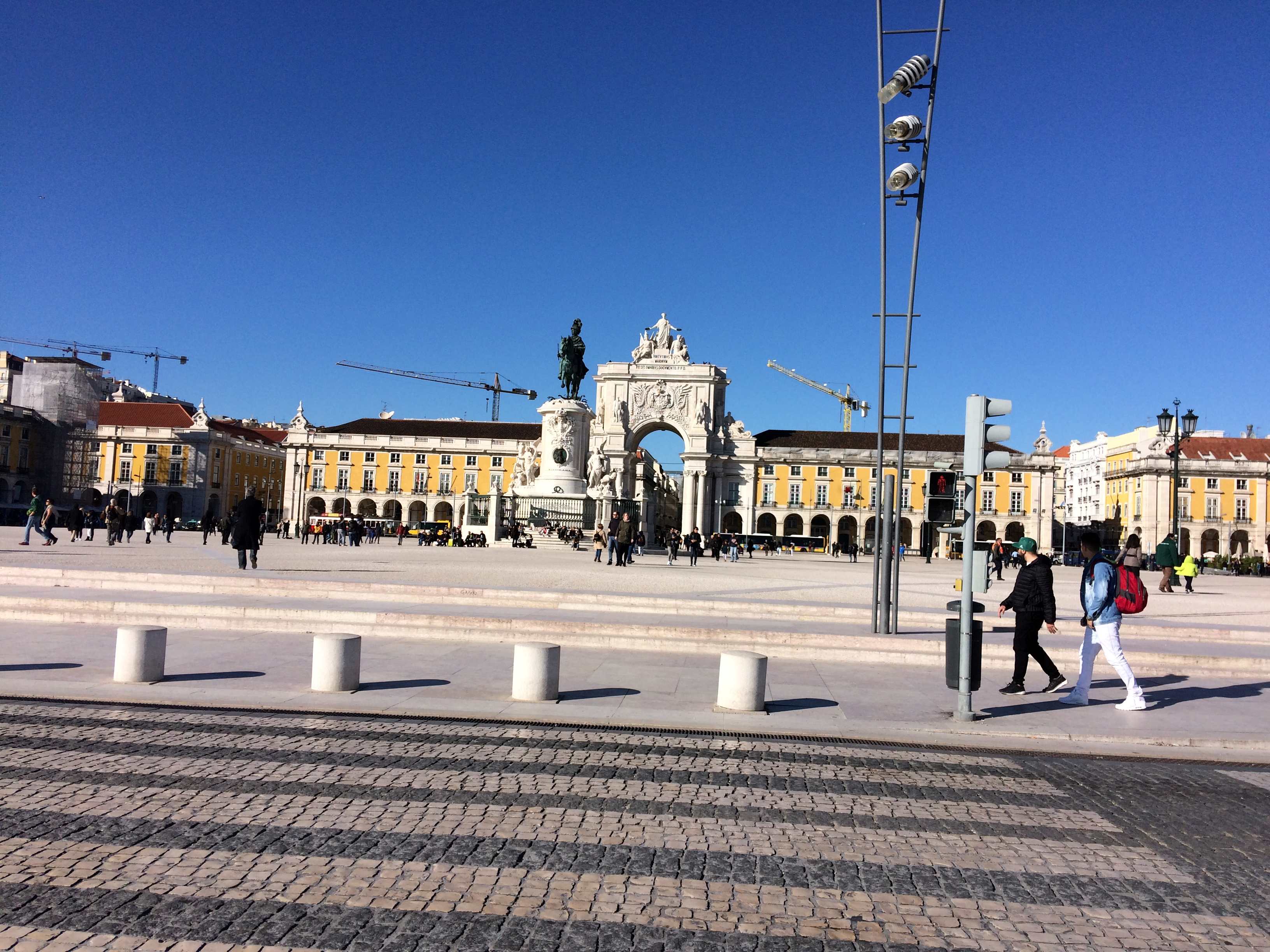 Fotografia do Terreiro do Paço e do Arco da Rua Augusta em Lisboa, com o chão em calçada portuguesa e o céu azul, simbolizando o centralismo político e administrativo de Portugal.